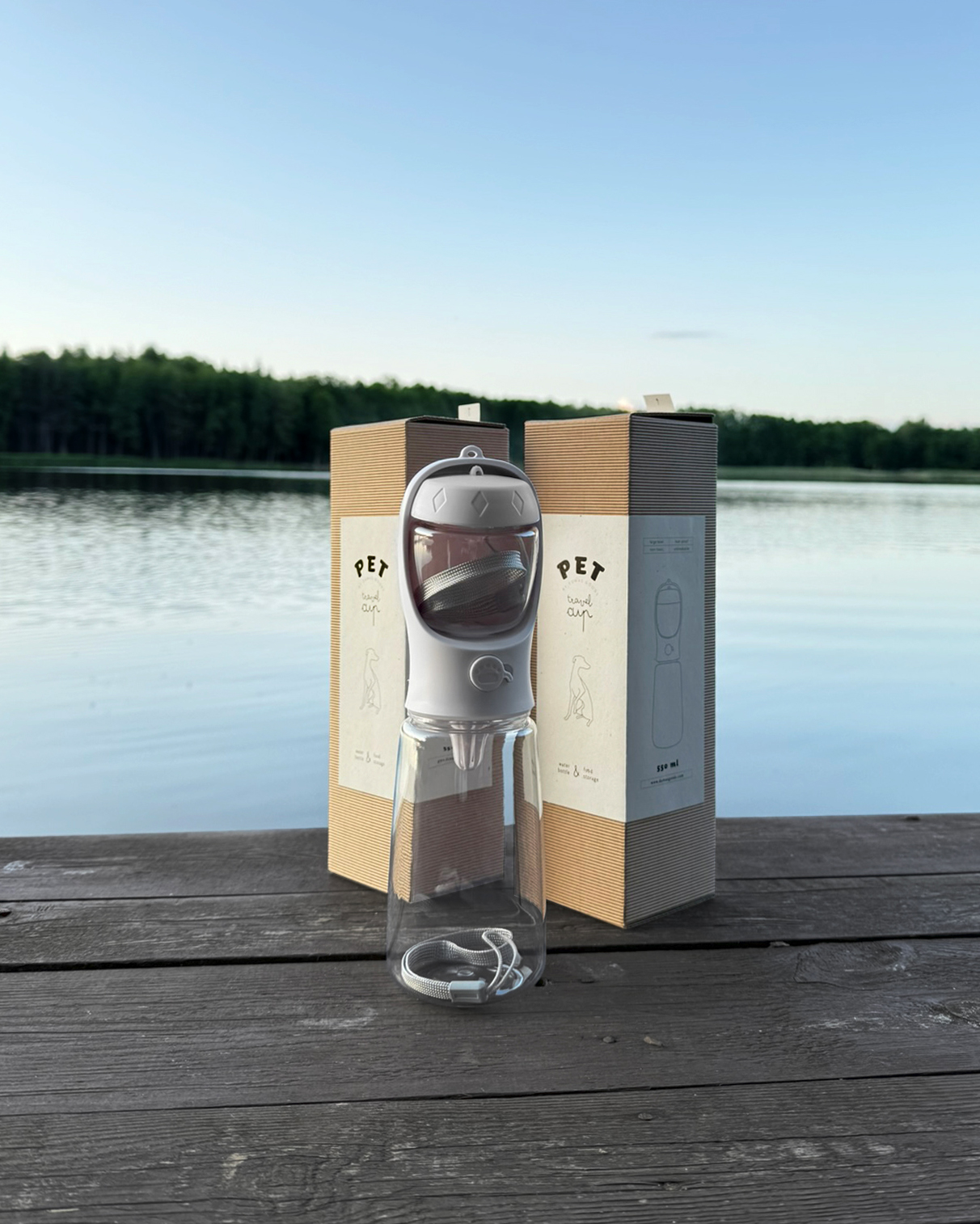 DumasGoods-pet-travel-water-bottle The white travel water bottle and it's packaging displayed on the edge of the wooden old footbridge at the lakeside in sunset